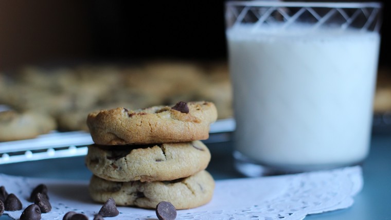 Close up on glass of milk and stack of chocolate chip cookies on doily